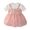 Girls pink pinafore party dress with white ribbed puff sleeve top, daisy flowers, pearl buttons and bubble skirt with bows – front view