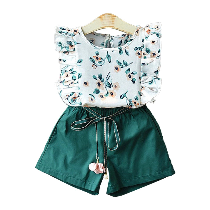 A two-piece children's outfit set on a wooden hanger against a white background. The set includes a sleeveless top with ruffled shoulders in a white base with a green and peach floral print, and solid dark green shorts with a drawstring waist and a small pink flower charm.