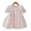 A toddler girl's short-sleeve dress with a pink and green floral print, featuring a lace-trimmed bodice, ruffled sleeves, and a layered tulle skirt, hanging on a wooden hanger against a white background.
